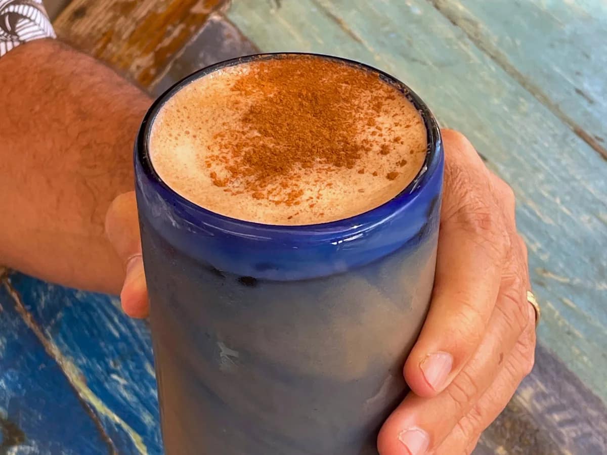 A hand around a blue glass of coffee topped with foam and a dusting of cocoa