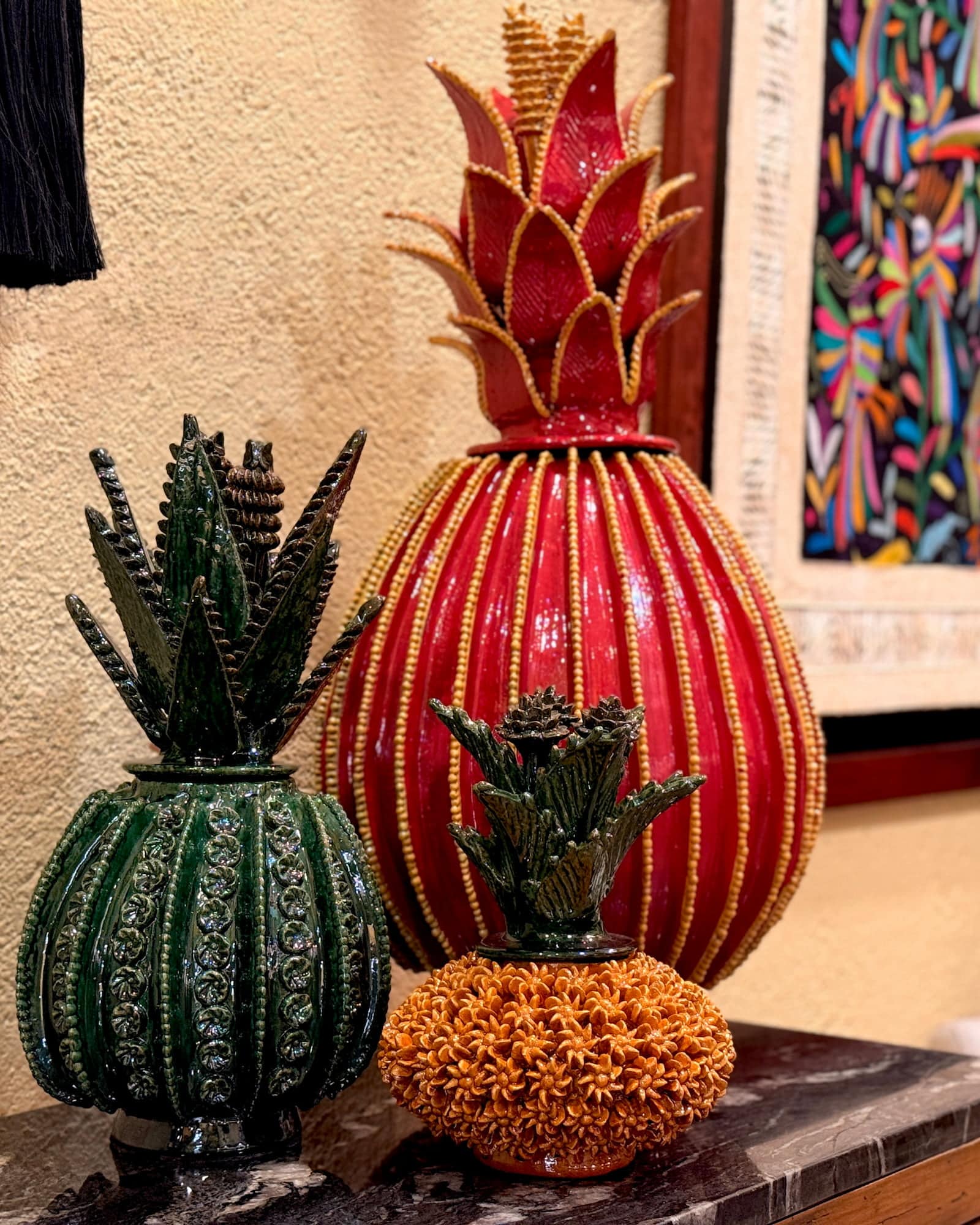Piñas y agaves de cerámica vidriada en rojo profundo y verde bosque sobre una repisa de mármol