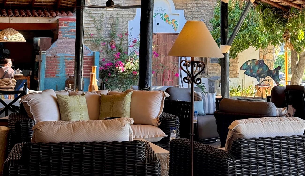 Terraza techada con sillones tejidos de exterior, cojines y un jardín de árboles en flor al fondo