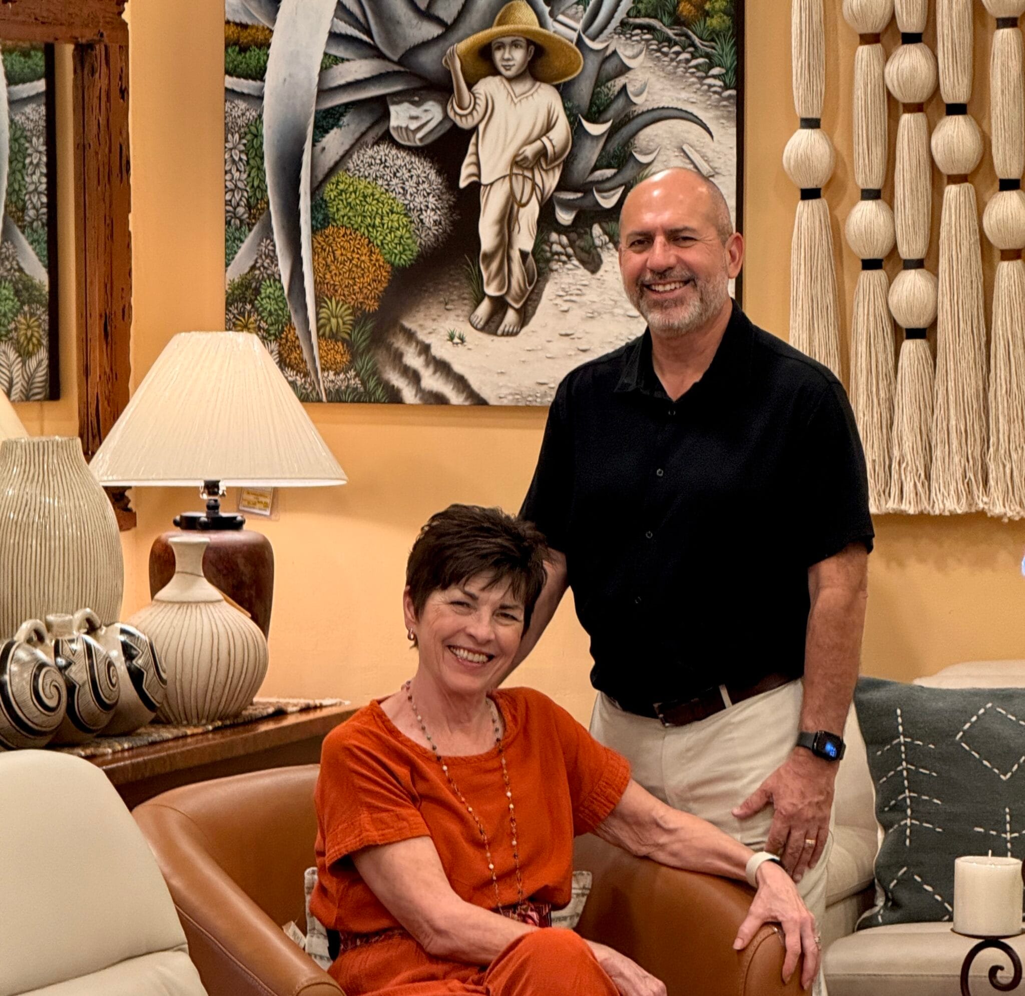 Marsha y Jorge, fundadores de Casa Bonita, en la tienda, junto a una lámpara tallada y un cuadro enmarcado