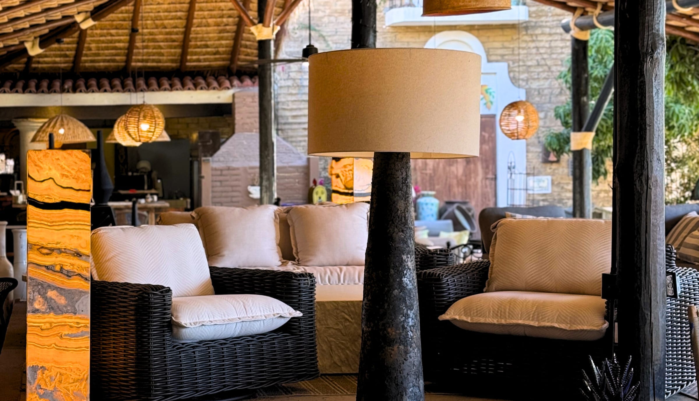 The covered showroom terrace at Casa Bonita, wicker armchairs and cushioned seating under a palapa roof hung with woven pendant lamps