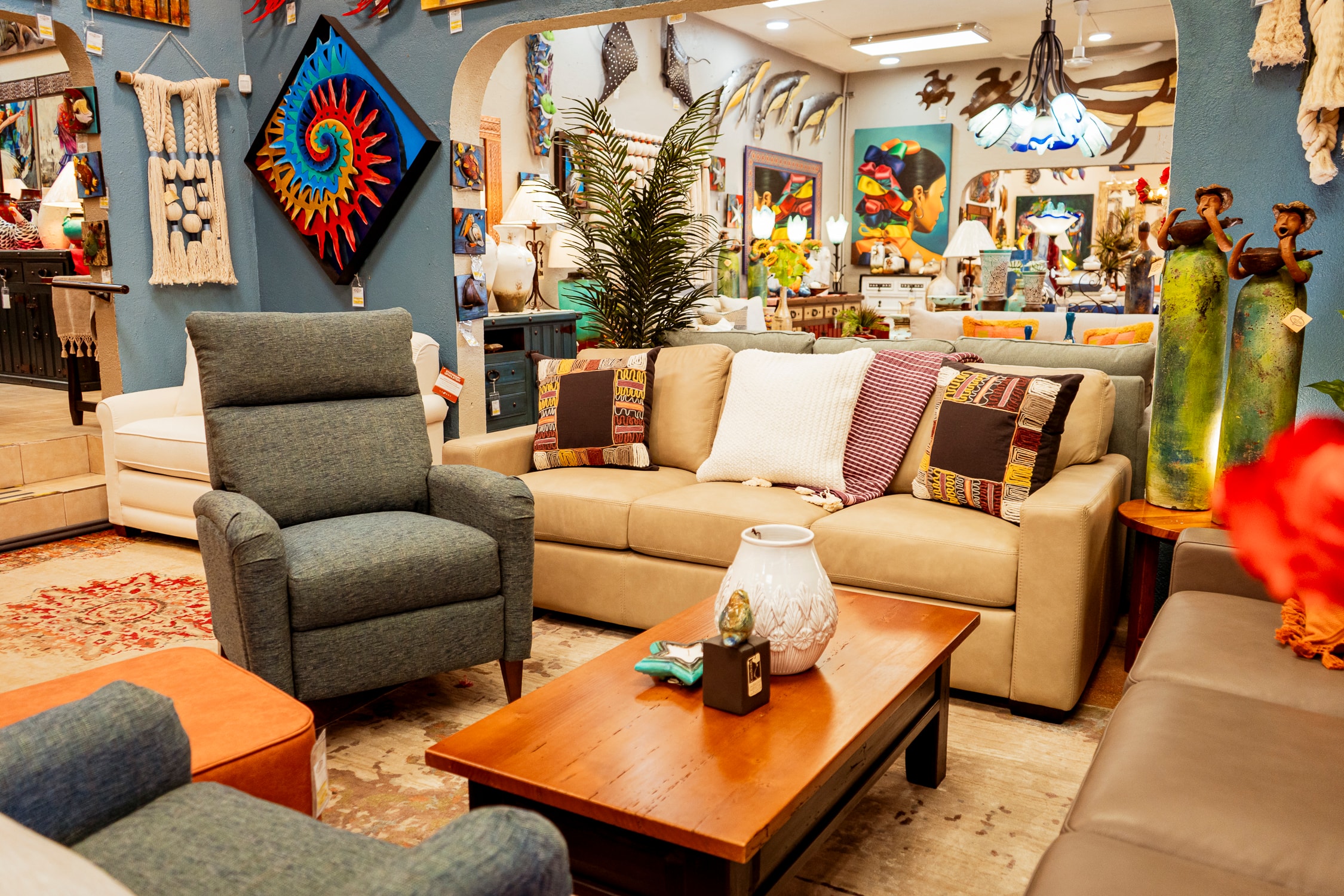 Casa Bonita showroom floor with layered seating, a carved coffee table, woven wall art and a painted sun sculpture