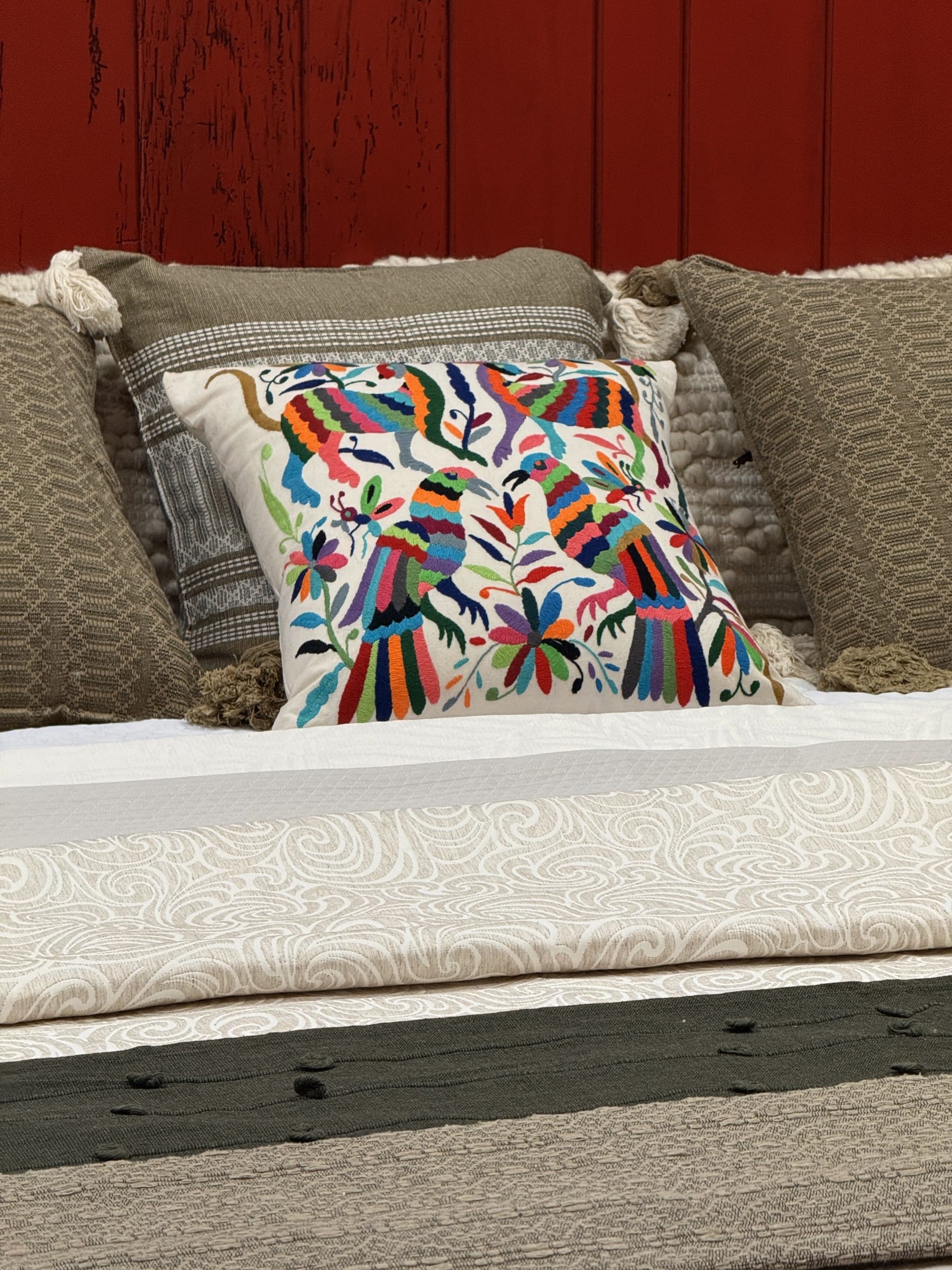 A multicolored Otomí embroidered pillow on a bed layered with woven coverlets