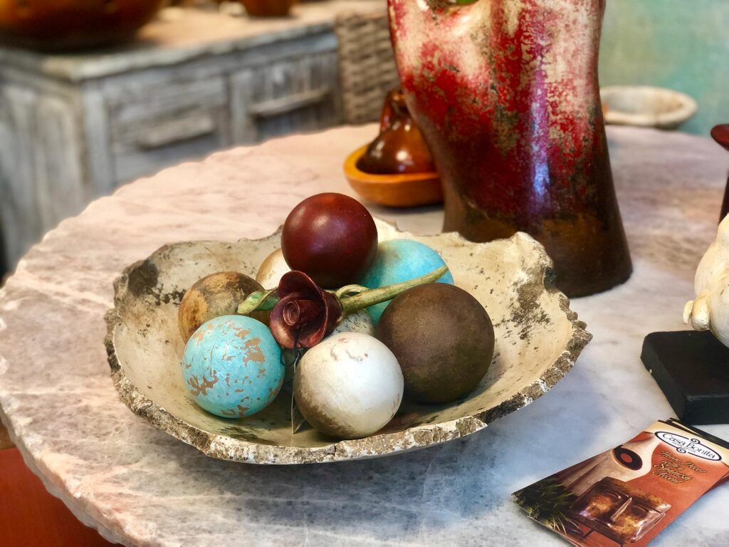 Decorative ceramic bowl with brown, white, blue, and red ceramic spheres and rose sitting on top of a coffee table
